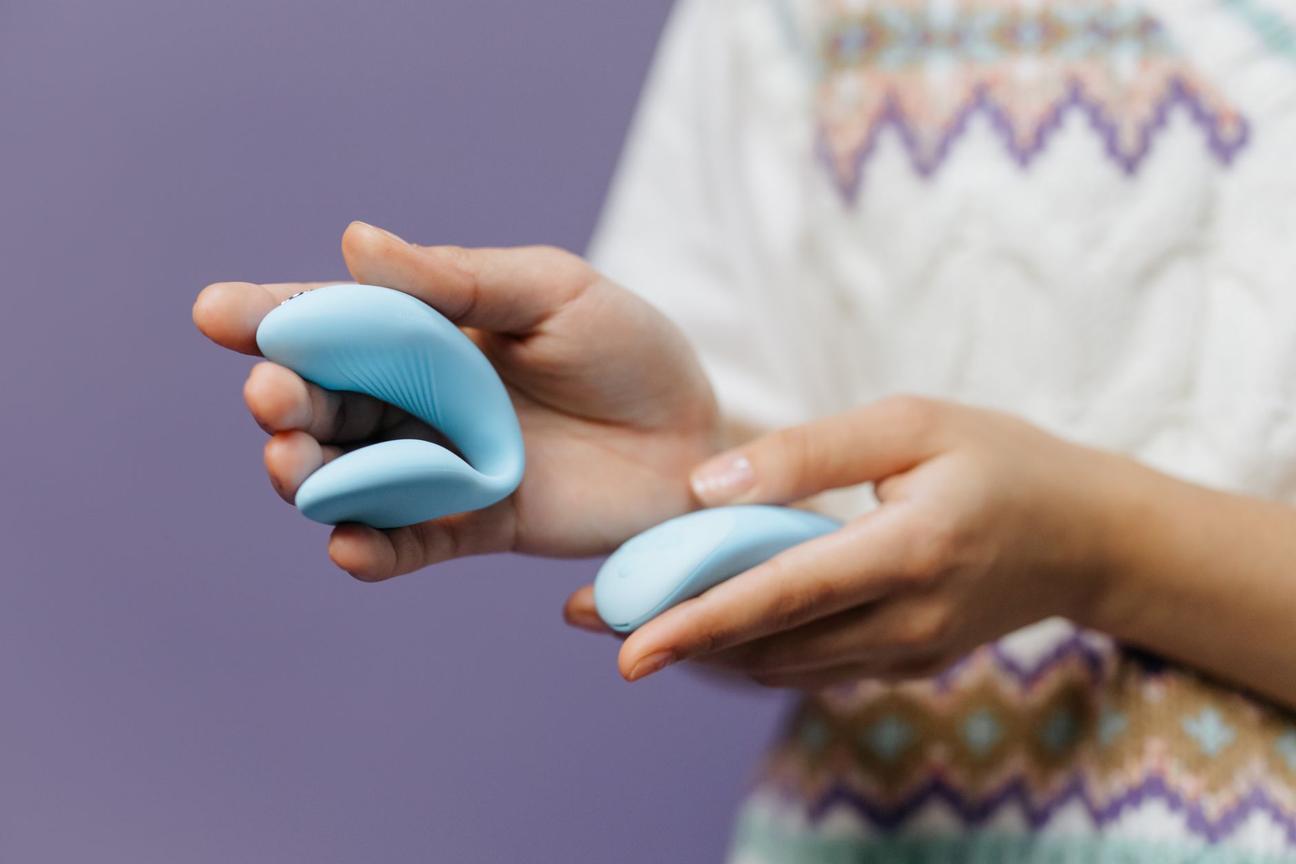 Close-up of hands holding a sleek blue vibrator against a purple background, representing intimate pleasure.